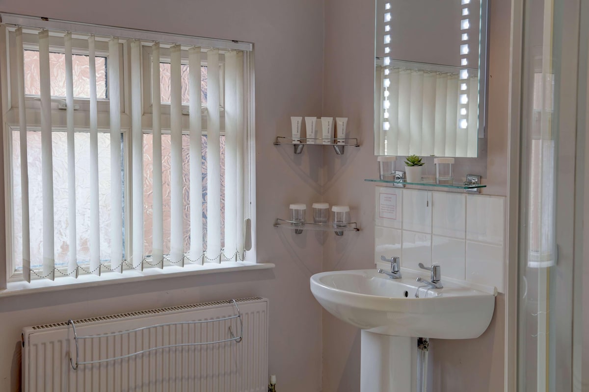 A bathroom with a window, radiator, sink, mirror, and toiletries shelf.