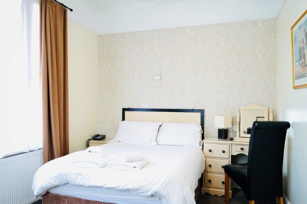 Une chambre d’hôtel comprenant un lit, une table de chevet, une chaise et un bureau avec un miroir.