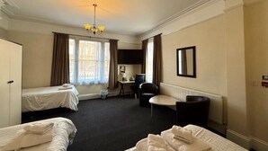 A hotel room with two beds, a desk, a chair, a radiator, and a chandelier. -  Deincourt Hotel (Newark)