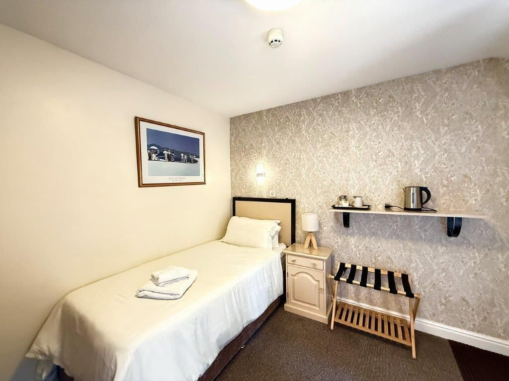 Habitación de hotel con cama, mesita de noche, estante con una tetera y un cuadro en la pared.