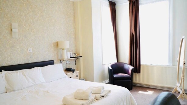 A hotel room with a large bed, a chair, a lamp, and a window with curtains. -  Deincourt Hotel (Newark)