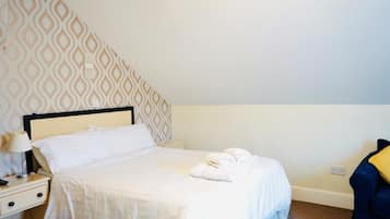 Una cama bien hecha con sábanas blancas, una lámpara de noche y una toalla sobre la cama.
