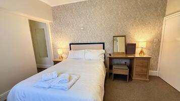 A hotel room with a bed, bedside table, lamp, and a mirror.