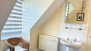 A bathroom with a white radiator, a white sink, a wicker chair, and a window with blinds. -  Deincourt Hotel (Newark)