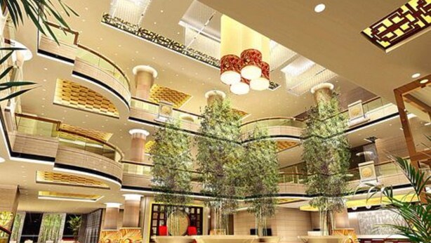 Un moderno vestíbulo de hotel con varios pisos, un atrio central con árboles y una amplia zona de estar.