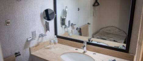 Un baño con lavamanos, espejo y toallero.