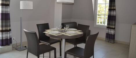 A dining area with a round table set for four, black chairs, a hanging light fixture, and a window with curtains.