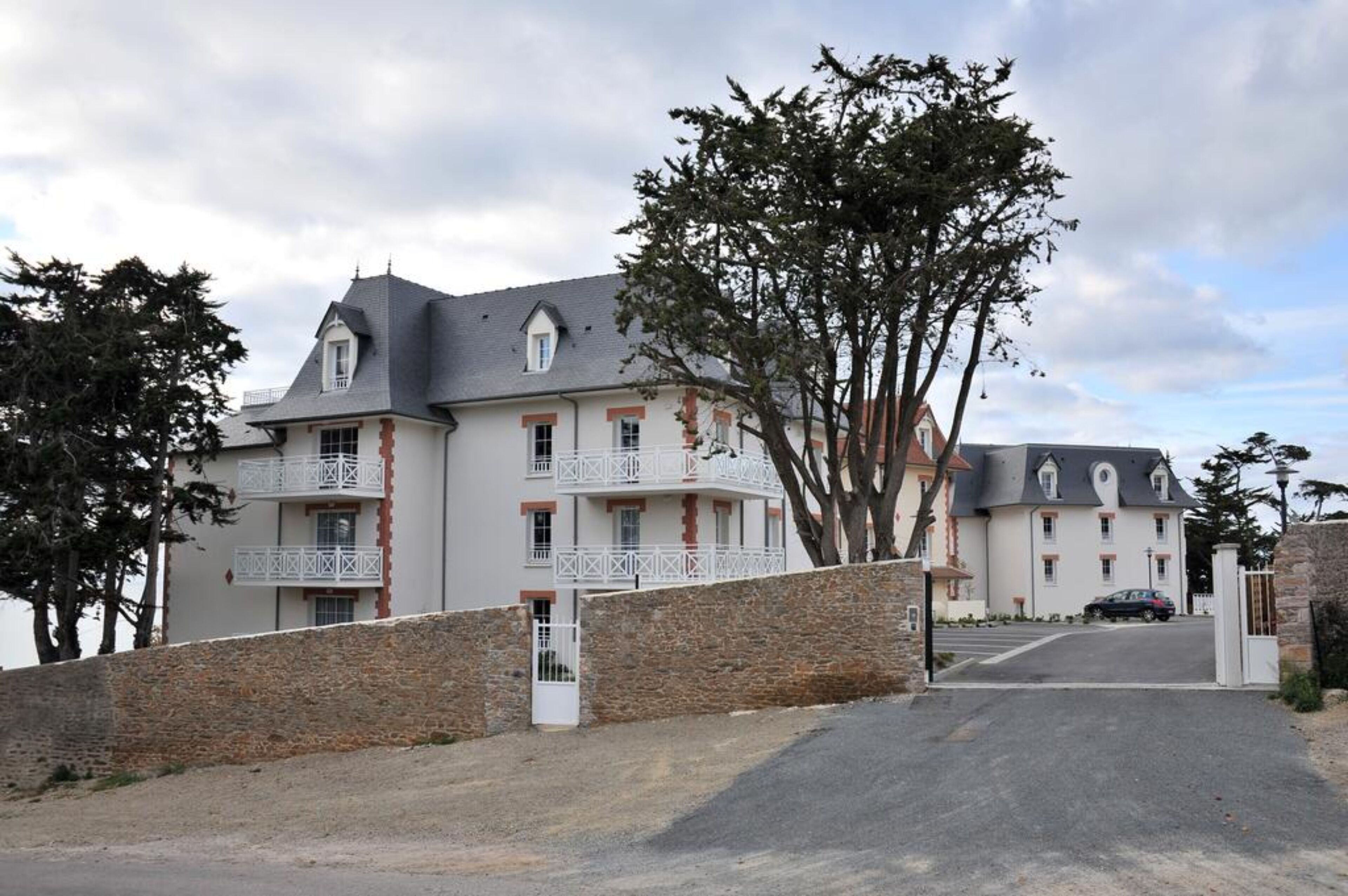 A two-story building with balconies, a stone wall, and a paved driveway.