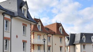 A multi-story residential building with a symmetrical facade, featuring a mix of brick and plaster exteriors, multiple balconies, and a variety of window styles. - Les Villas du Spa (Pleneuf-Val-Andre)