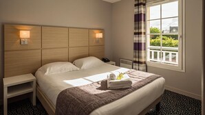 A hotel room with a large bed, bedside lamps, a nightstand, a window with curtains, and a view of greenery outside. - Les Villas du Spa (Pleneuf-Val-Andre)