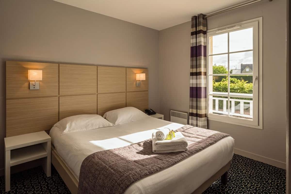 Une chambre d’hôtel avec un grand lit, des lampes de chevet, une table de chevet, une fenêtre avec des rideaux et une vue sur la verdure environnante.