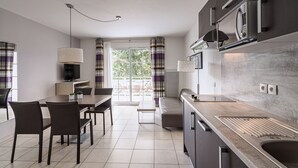 A modern kitchen with a built-in microwave, a dining area with a table and chairs, and a large window with curtains. - Les Villas du Spa (Pleneuf-Val-Andre)