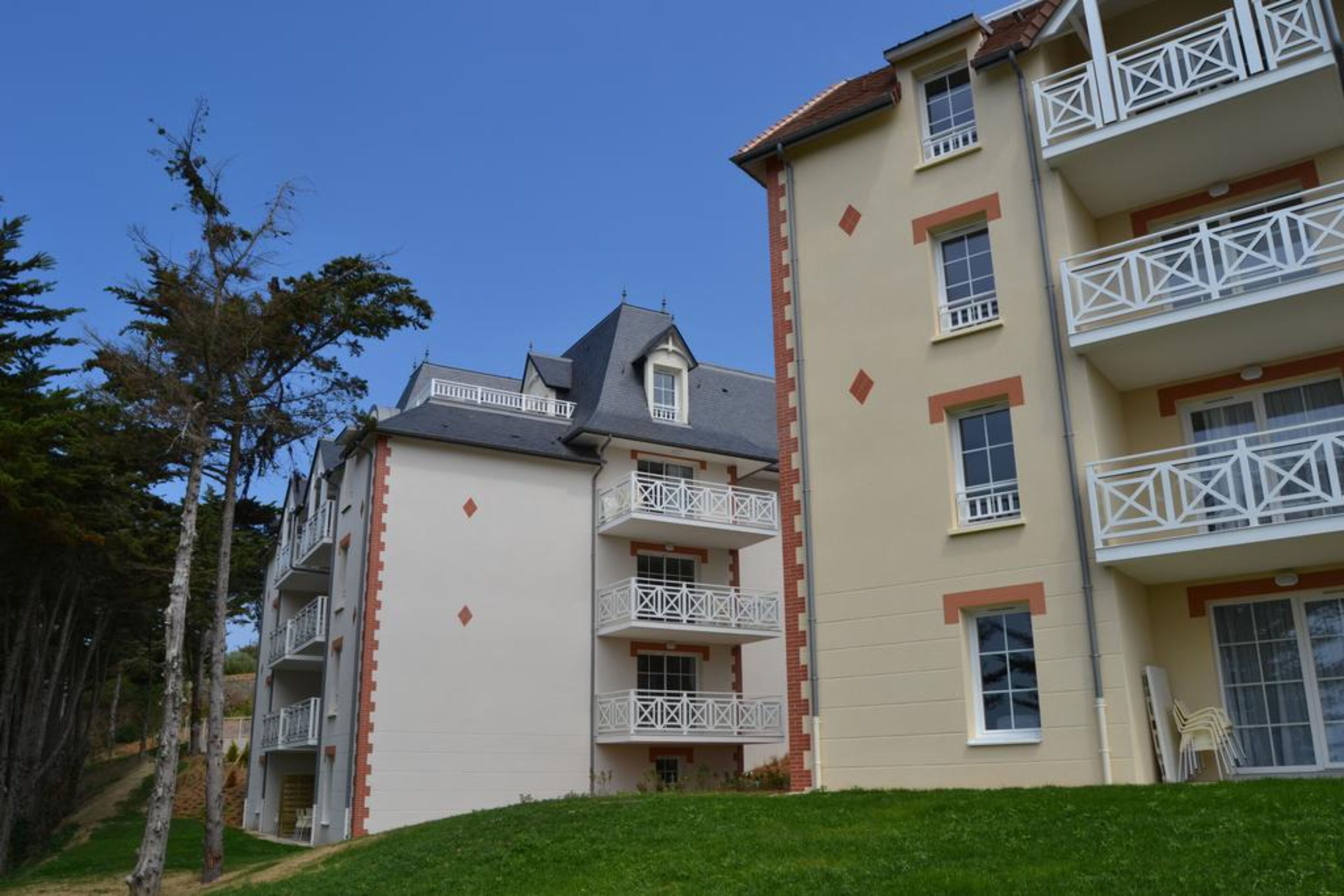 Un hôtel à plusieurs étages doté de balcons, d’un toit en pente et d’une pelouse bien entretenue.