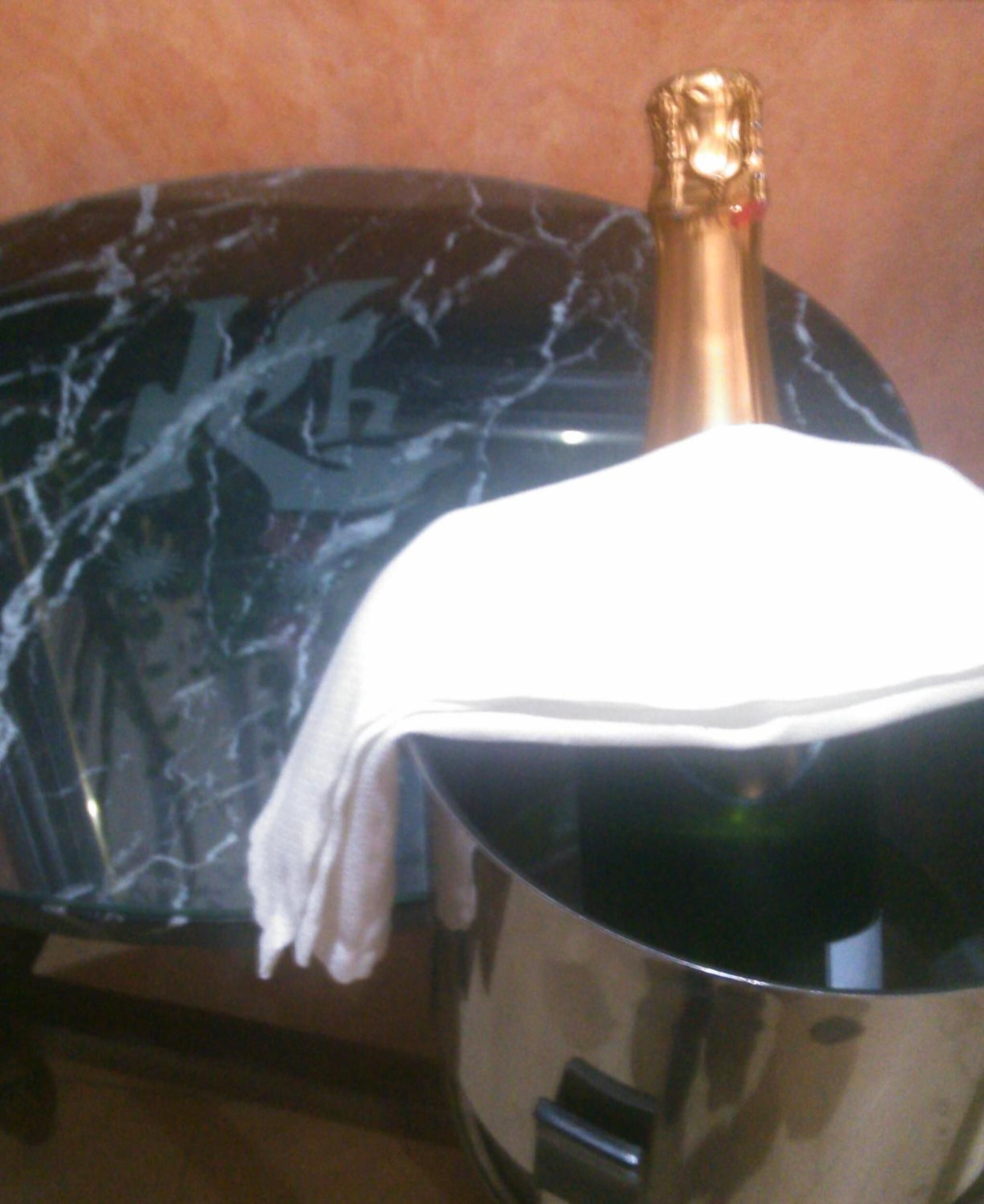 Una botella de champán cubierta con un paño blanco, colocada sobre una mesa junto a un plato con diseño de mármol negro.