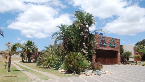 A building with a garage and a brick facade, surrounded by palm trees and a clear sky. - Bluewater Guesthouse (Gqeberha (Port Elizabeth))
