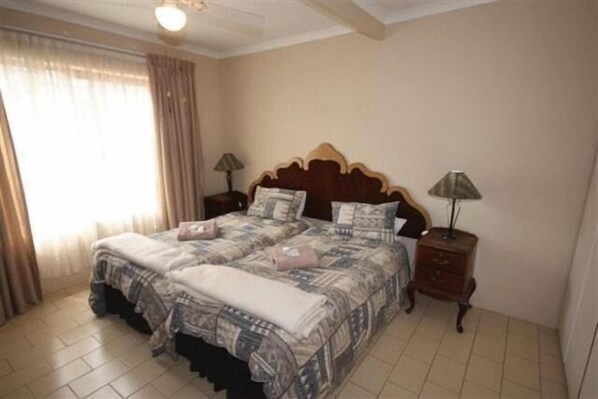 Una cama doble con una colcha estampada, dos mesitas de noche con lámparas y una ventana con cortinas.