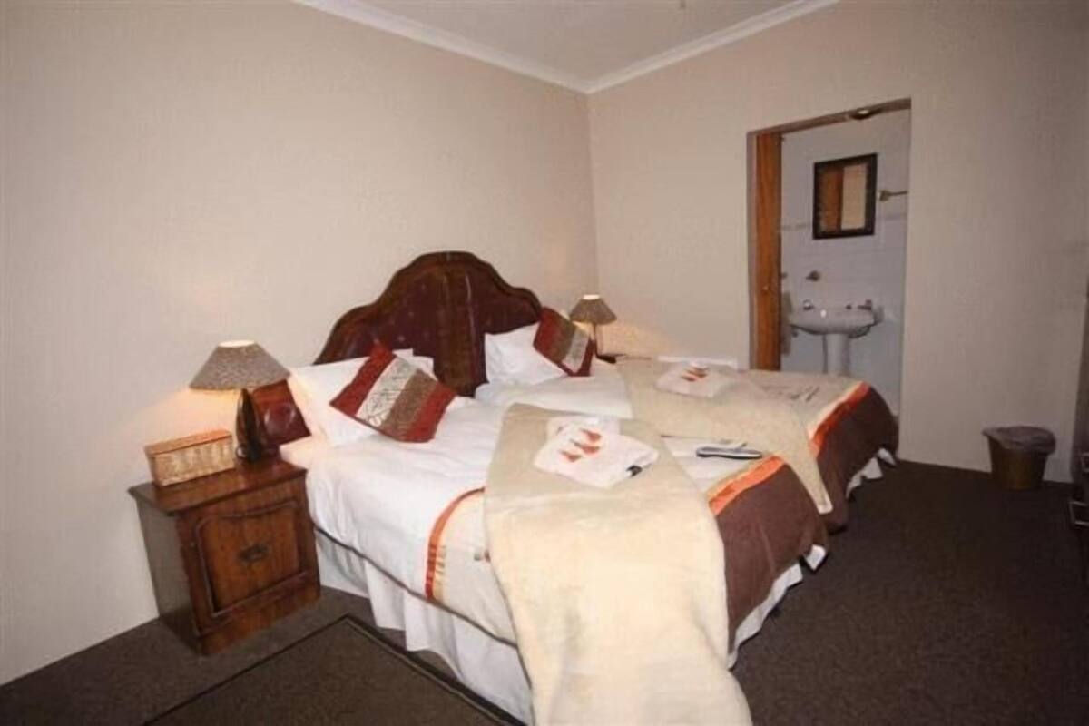 Una habitación de hotel con dos camas, una mesita de noche con lámpara, un armario pequeño y un baño con lavabo y espejo.