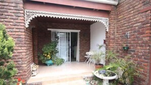 A brick building with a covered entrance, steps leading up to a door, and potted plants around the entrance area. - Bluewater Guesthouse (Gqeberha (Port Elizabeth))