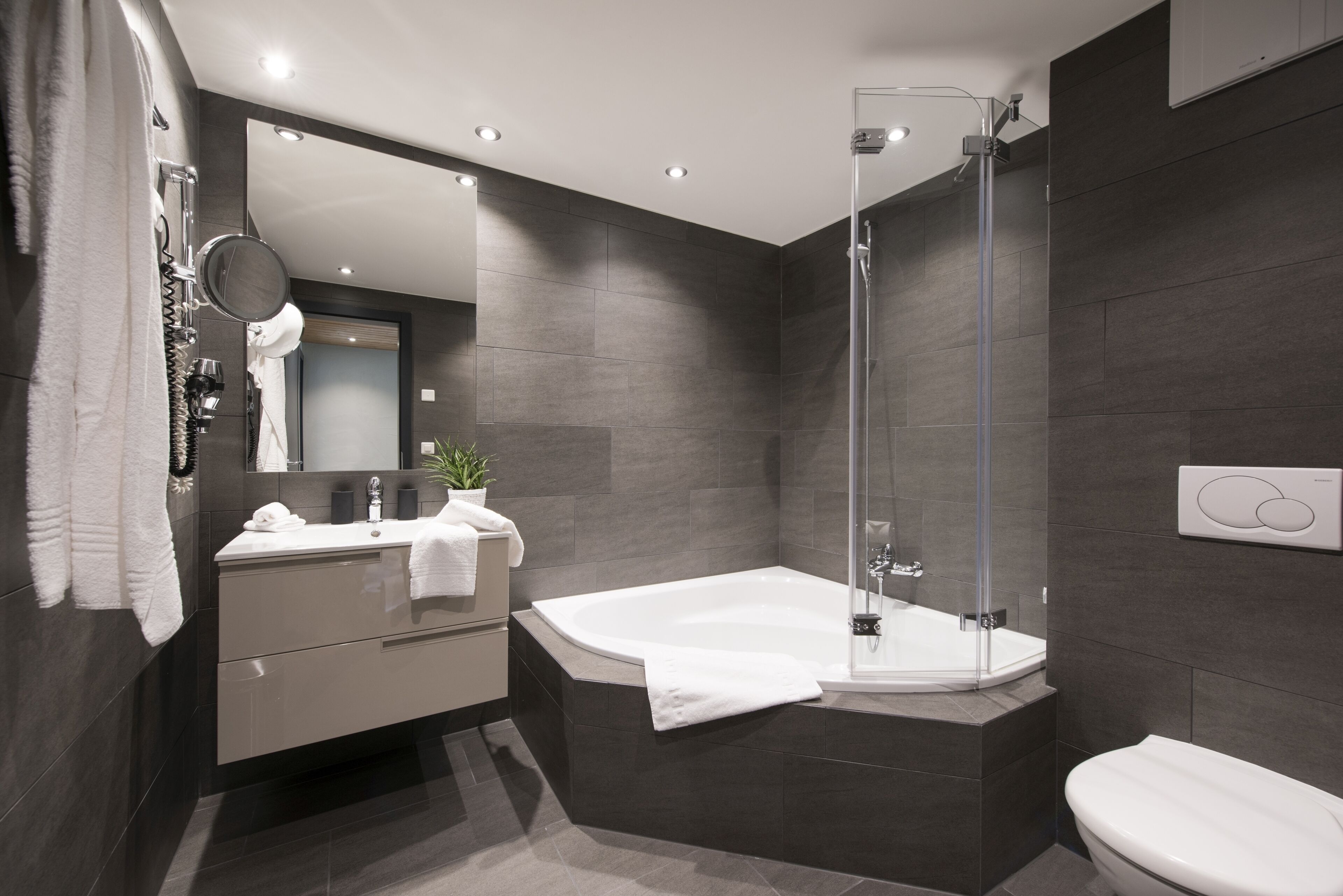 Een moderne badkamer met een bad, een douche met glazen wanden, een wastafel met spiegel en een toilet.