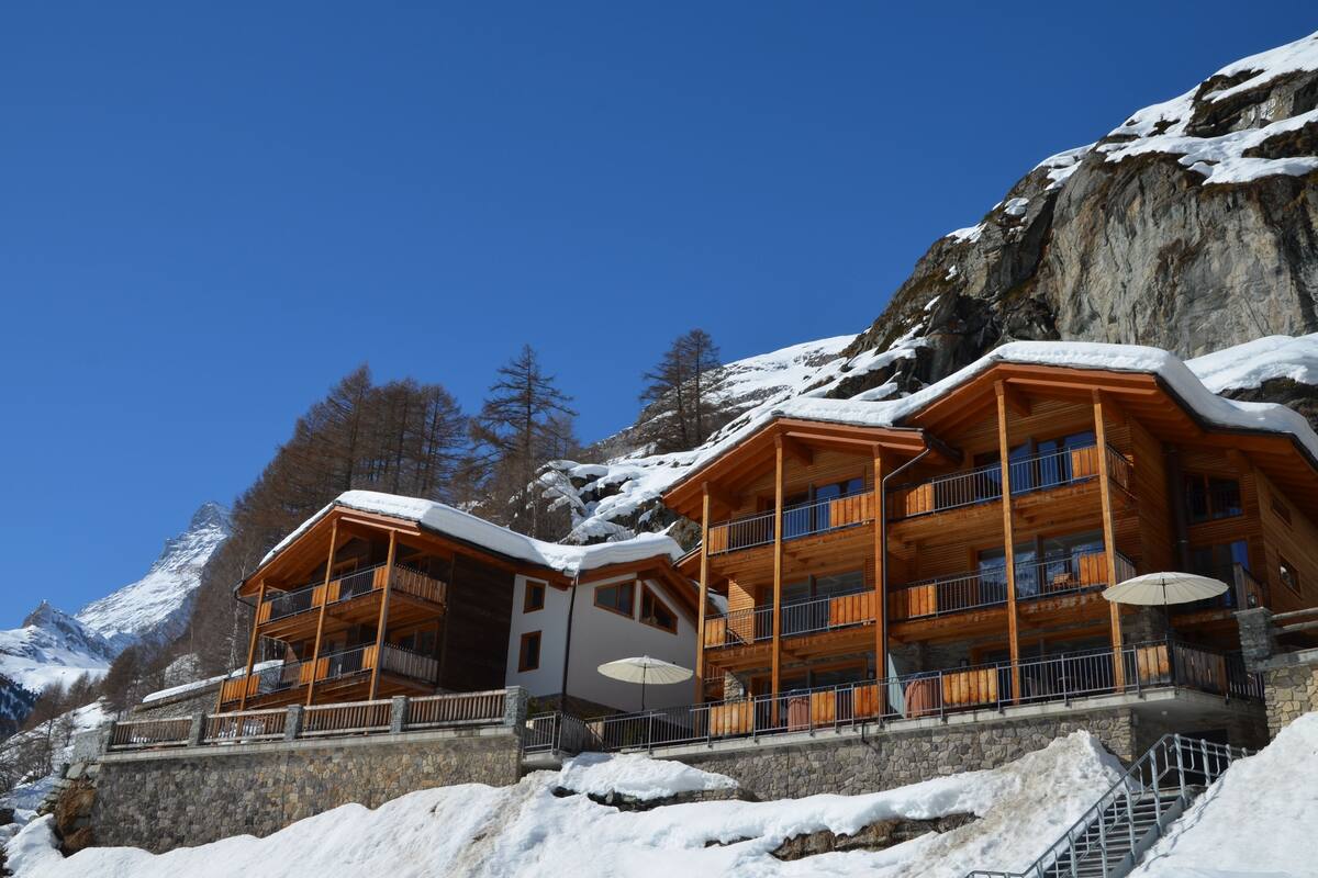 A multi-story wooden lodge with balconies, set against a snowy mountain backdrop.