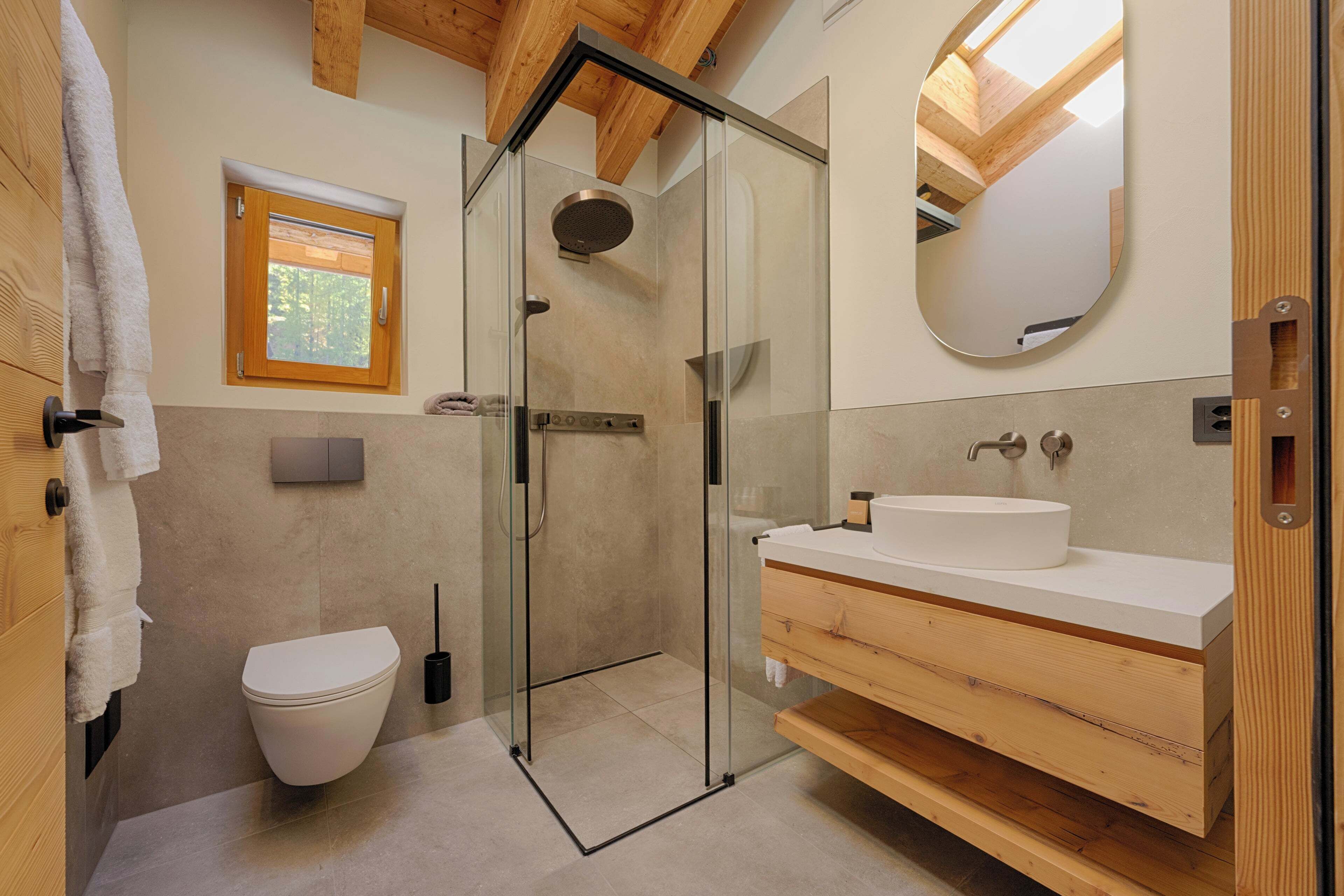 Ein modernes Badezimmer mit einer Glasdusche, einer weißen Toilette und einem Holzwaschtisch.