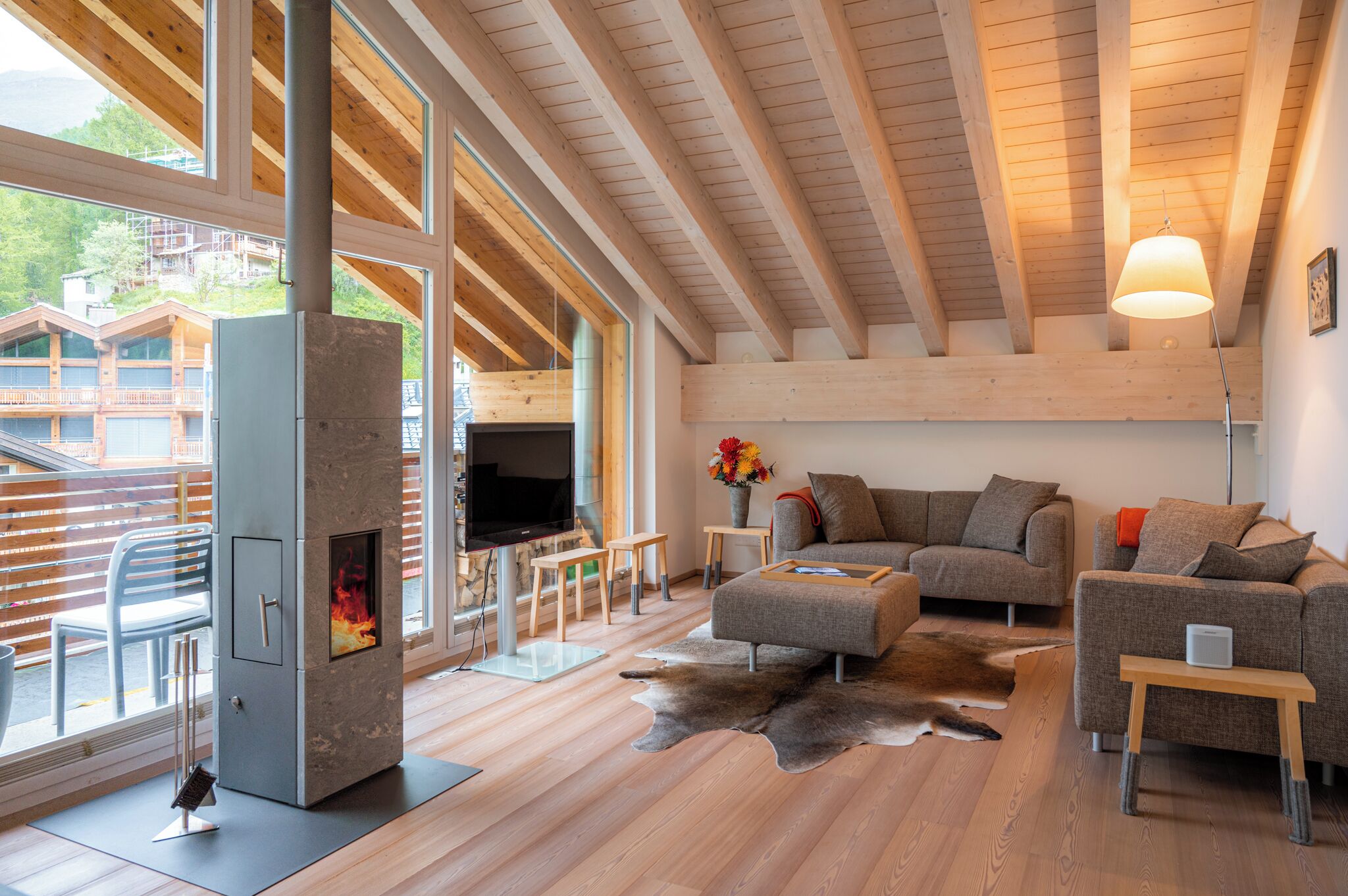A modern living room with a stone fireplace, wooden beams, large windows, and a sofa.
