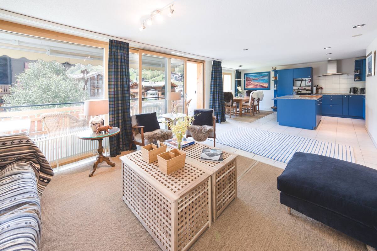 A modern living room with a sofa, a coffee table, and a dining area with chairs and a table.