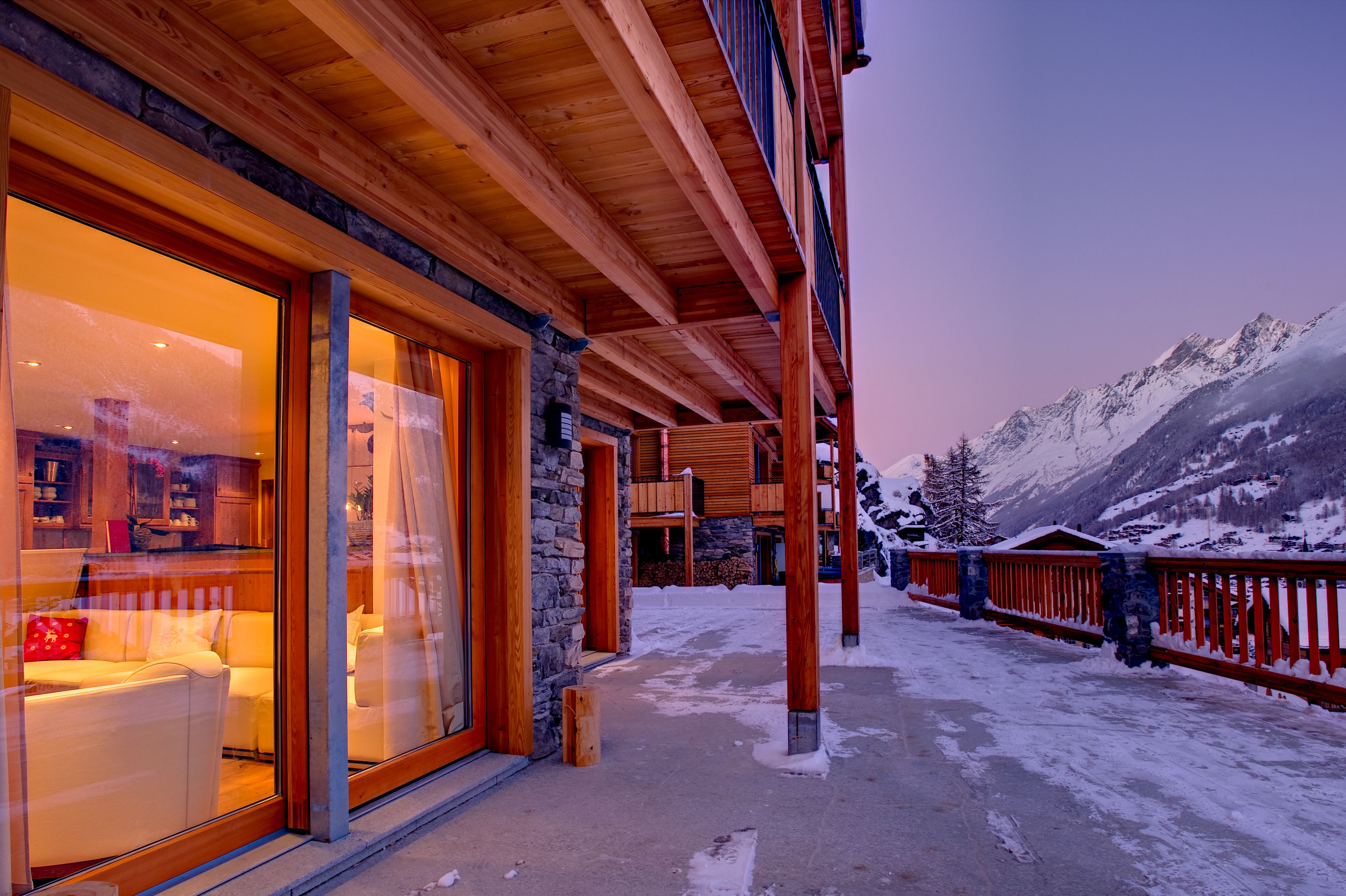Ein Holzhaus mit großen Glasfenstern, einer Steinfassade und Blick auf schneebedeckte Berge.