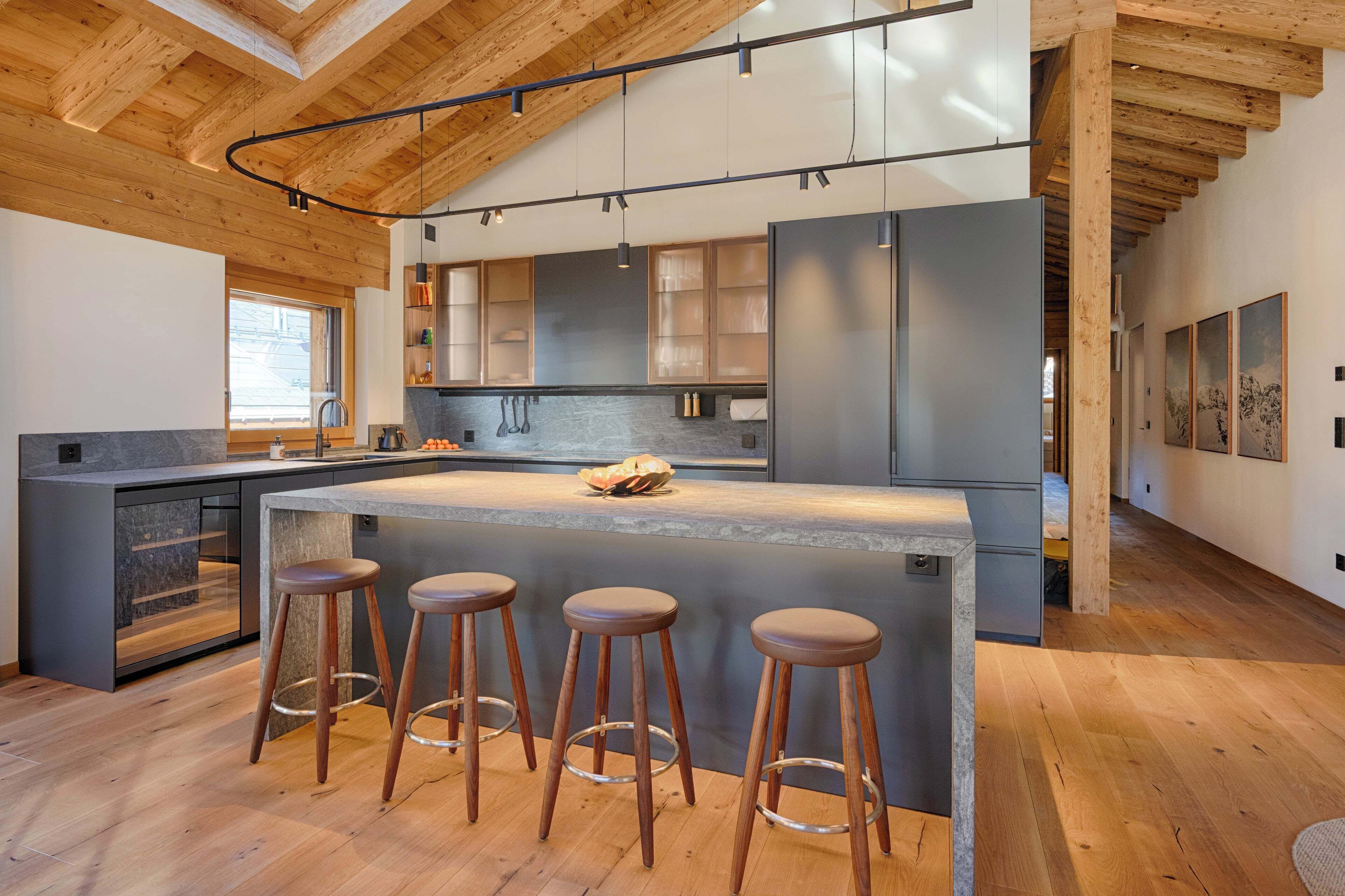 Une cuisine moderne dotée d’un grand îlot central, de tabourets de bar et de poutres en bois au plafond.