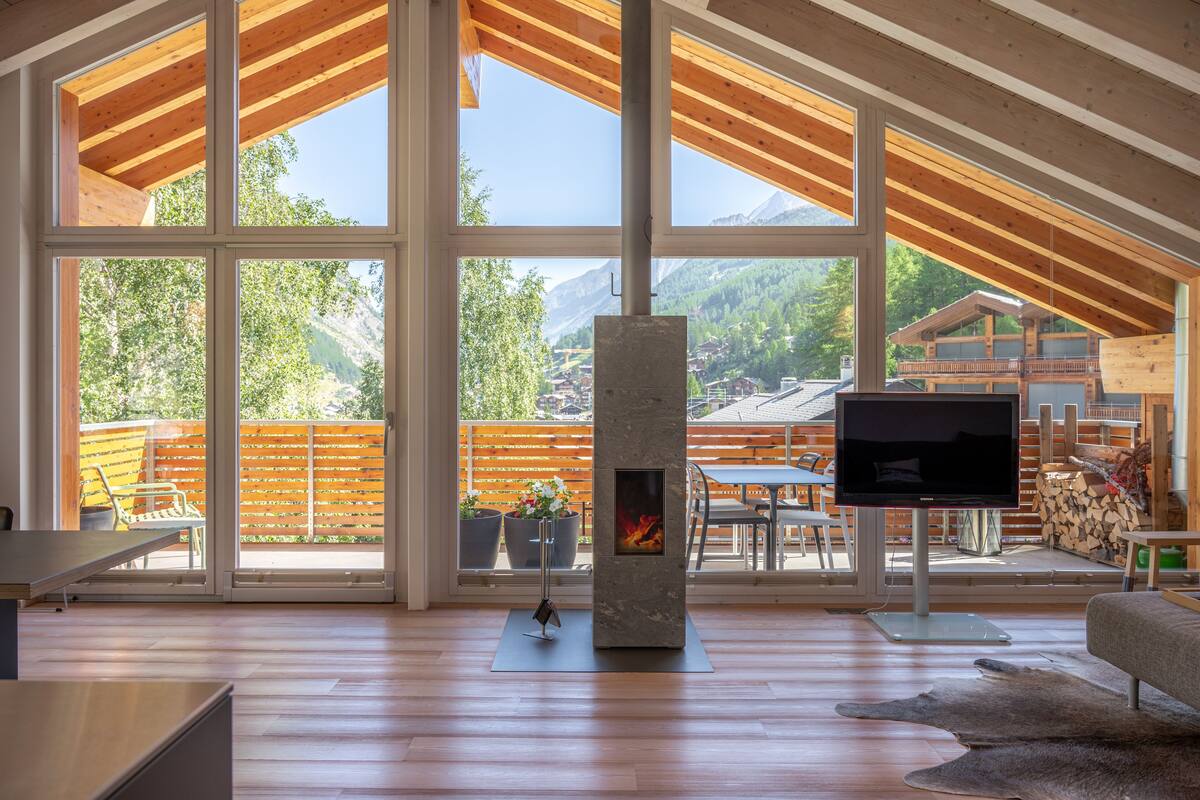 A spacious living area with a large fireplace, wooden beams, and a view of mountains.