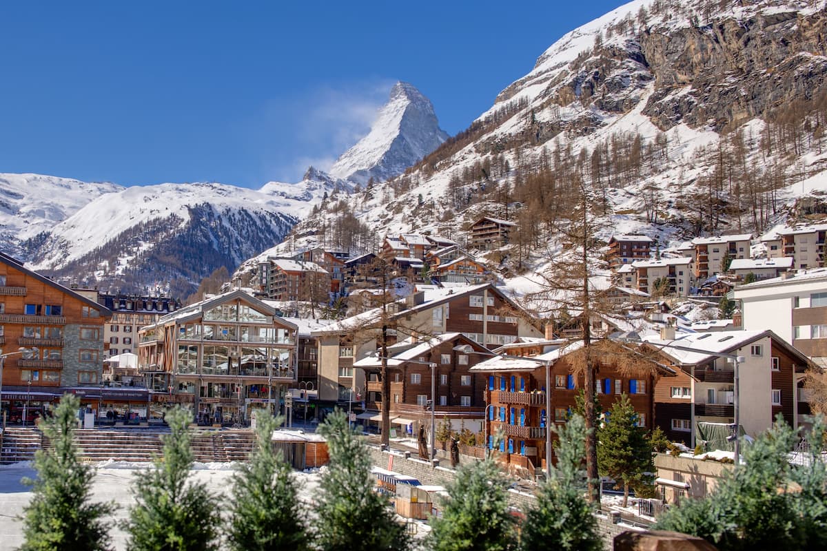 A snow-covered mountain town with wooden buildings and a prominent mountain peak in the background.