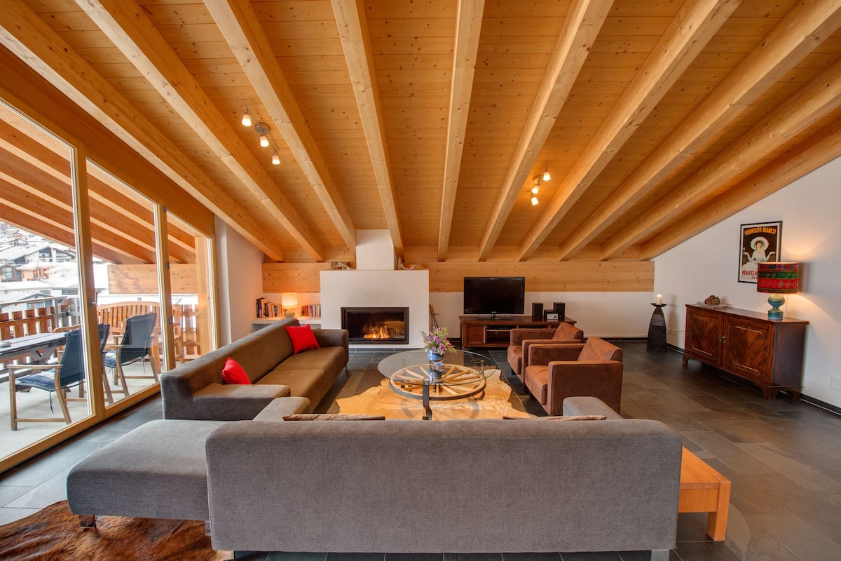 A spacious living area with a fireplace, large windows, and wooden beams.