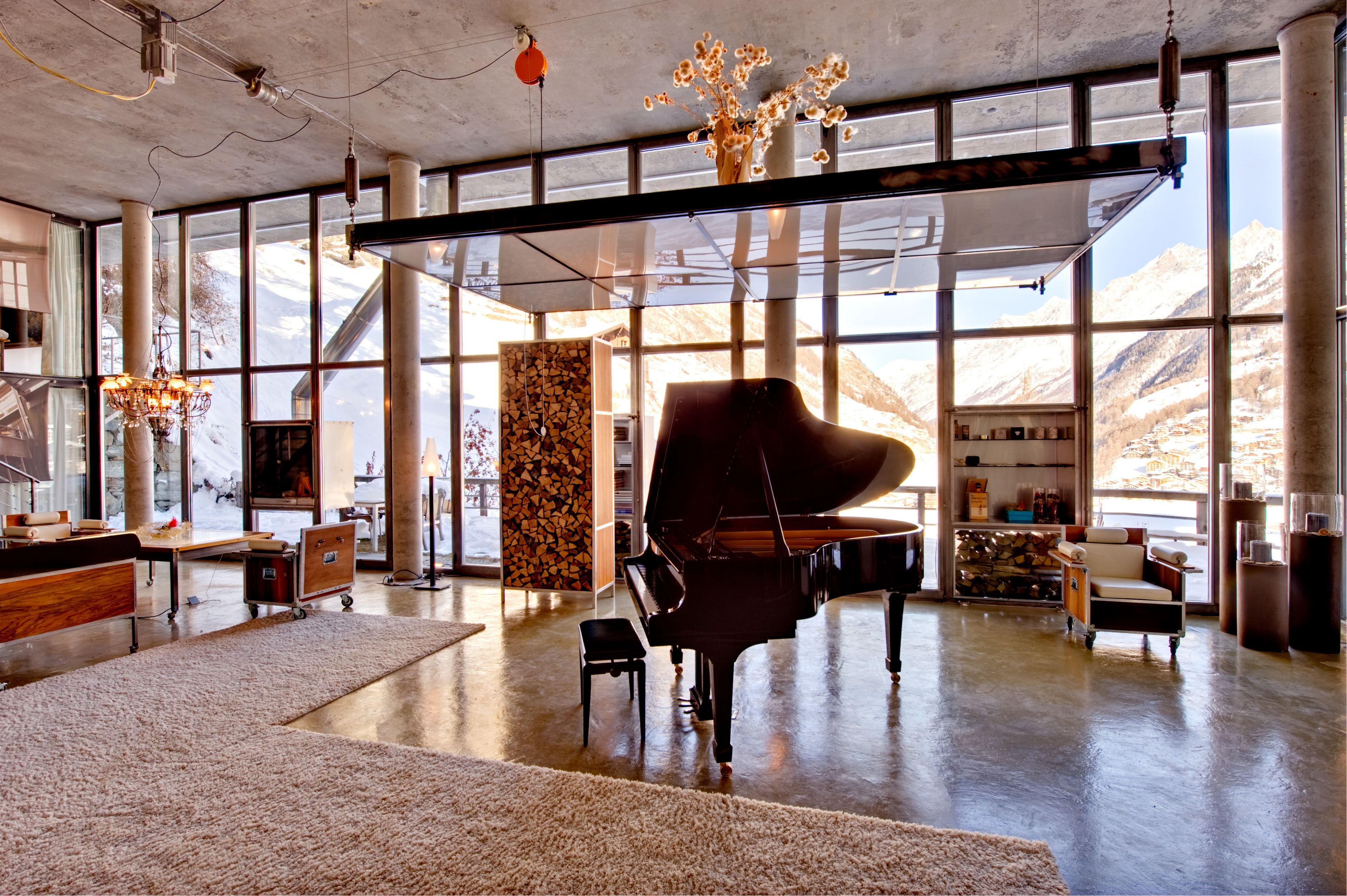 Une pièce spacieuse avec un grand piano, de grandes fenêtres offrant une vue sur les montagnes et un lustre moderne.