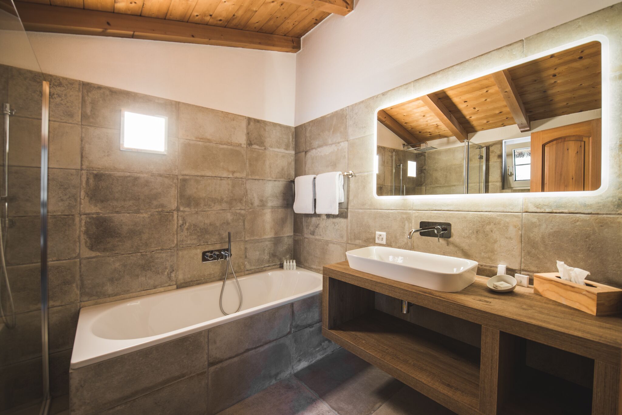 A modern bathroom with a large bathtub, a wooden vanity, and a large mirror.