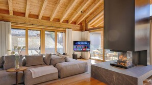 Una sala de estar moderna con techo de madera, un televisor de pantalla plana grande, una chimenea y un sofá.