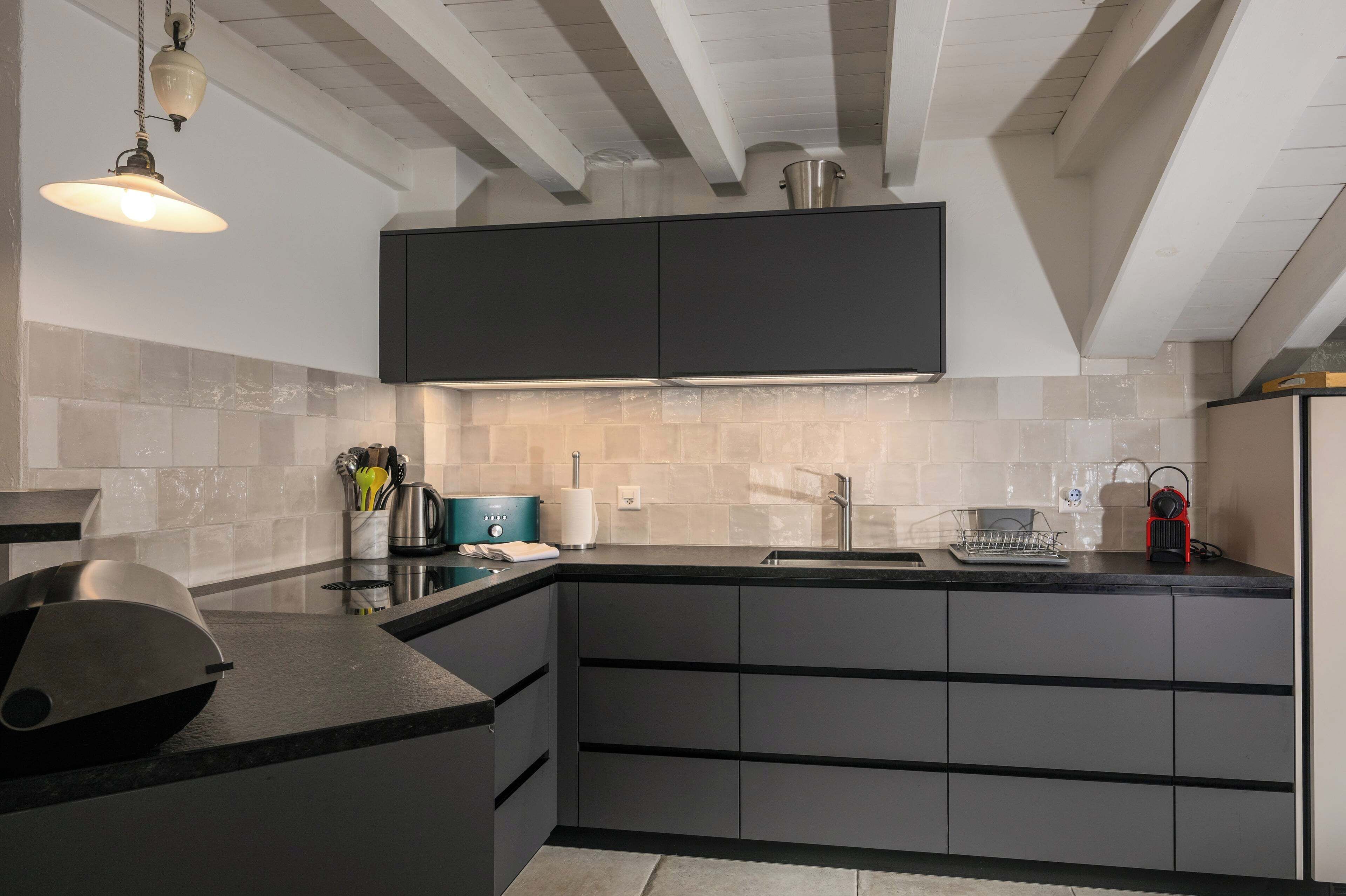 Une cuisine moderne avec des meubles de couleur sombre, un évier en acier inoxydable et un plan de travail noir.