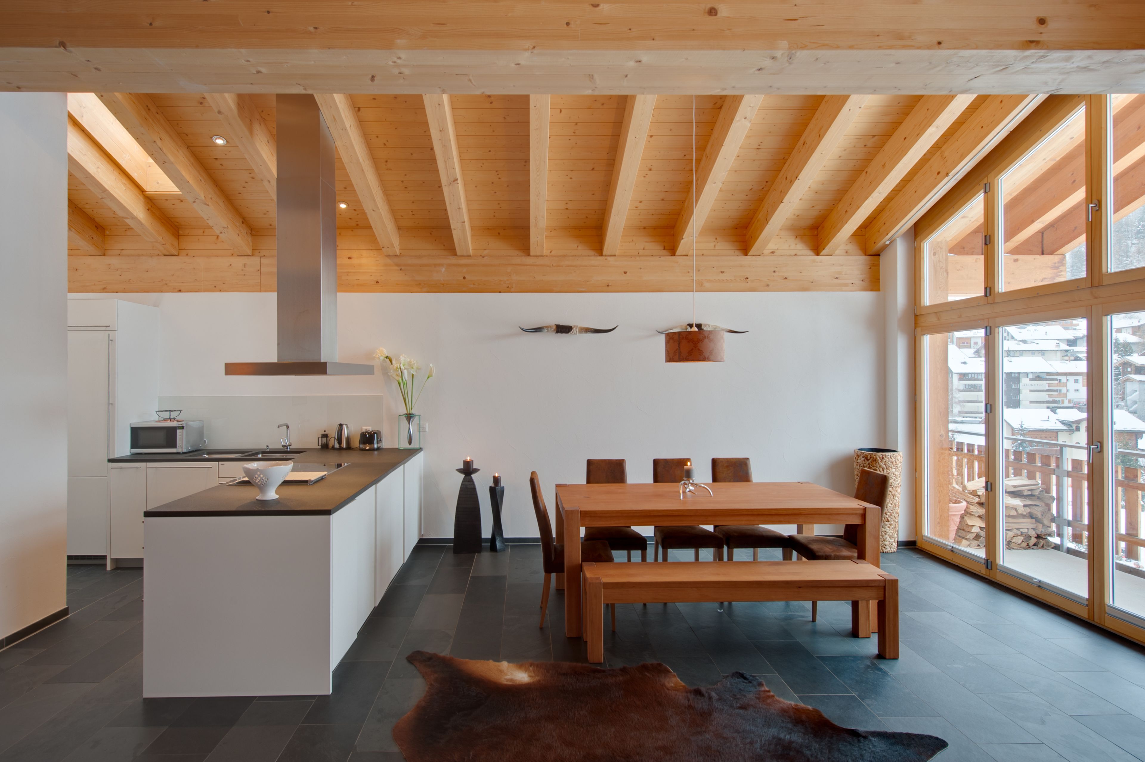 A modern kitchen with a central island, wooden dining table, and chairs.