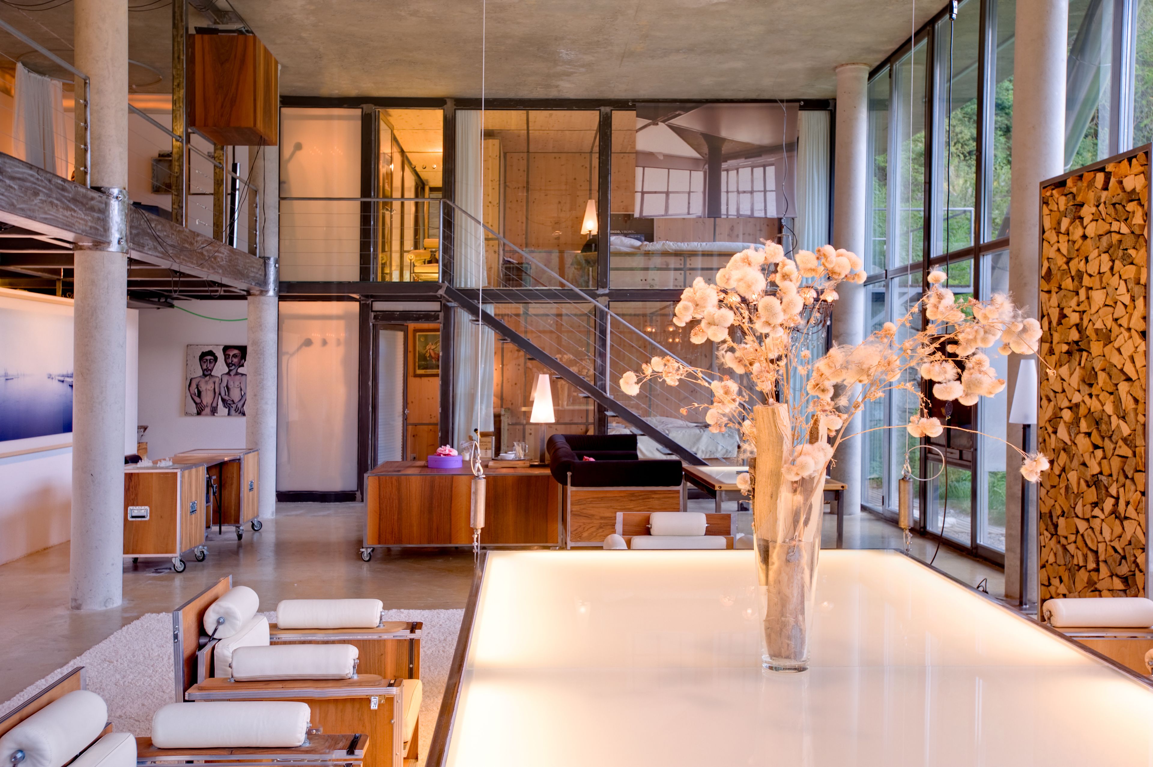 Eine moderne Hotelhalle mit einer großen Glaswand, einer Treppe und einem zentral platzierten Tisch mit Blumen.