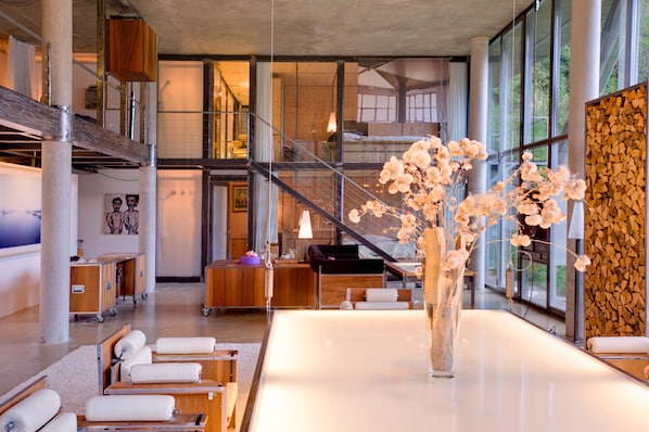 A modern hotel lobby with a large glass wall, a staircase, and a central table with a vase of flowers. - Luxury Chalets & Apartments by MX Zermatt (Zermatt)