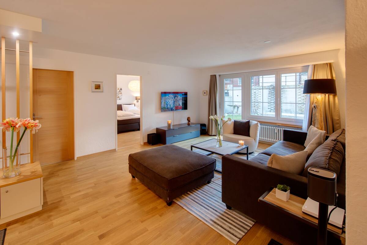 A modern living room with a sofa, ottoman, coffee table, and a TV mounted on the wall.