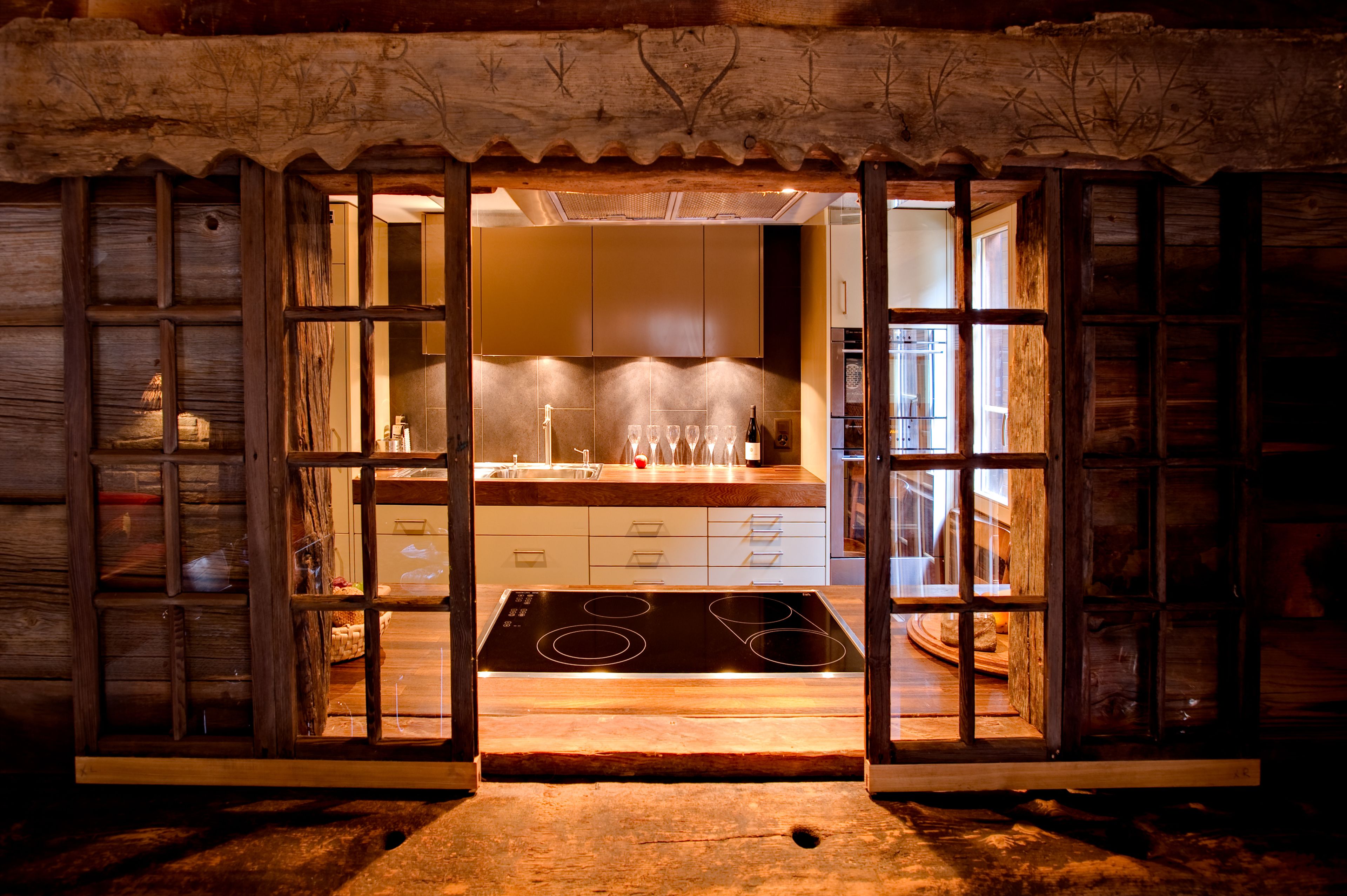 A rustic kitchen with wooden walls, a modern stove, and a view into the adjacent dining area.