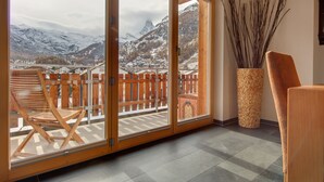 Una habitación con una silla de madera, un ventanal con vistas a montañas nevadas y un jarrón decorativo.