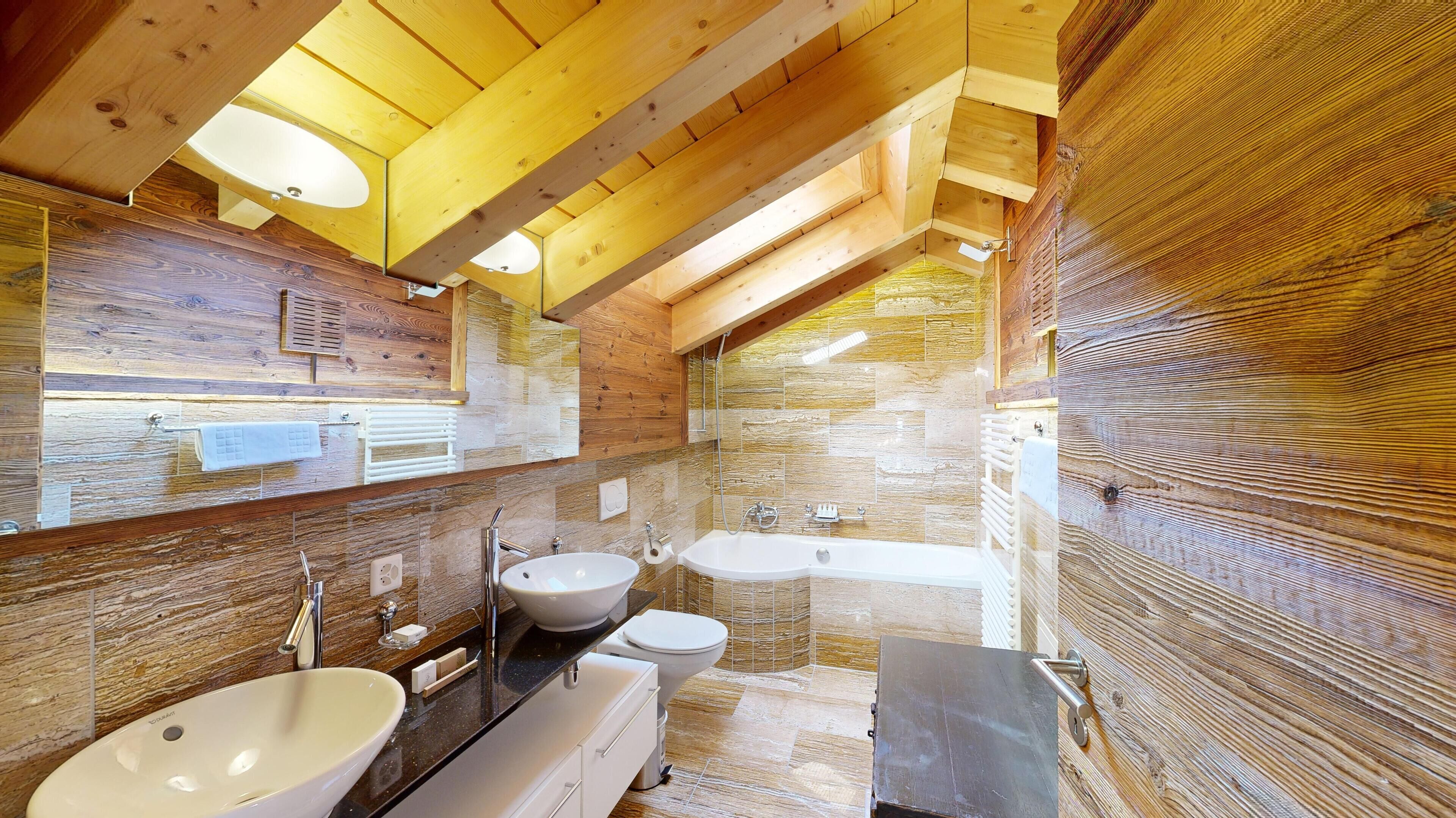 A modern bathroom with a wooden ceiling, a large mirror, a sink, a toilet, and a bathtub.