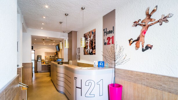 A hotel reception area with a modern design, including a reception desk labeled "H21" and a large wall art piece. - Le 21 Hotel (Saint-Raphael)