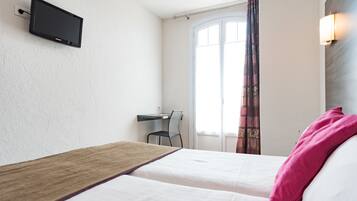 Een hotelkamer met twee bedden, een bureau, een stoel, een aan de muur bevestigde televisie en een raam met gordijnen.