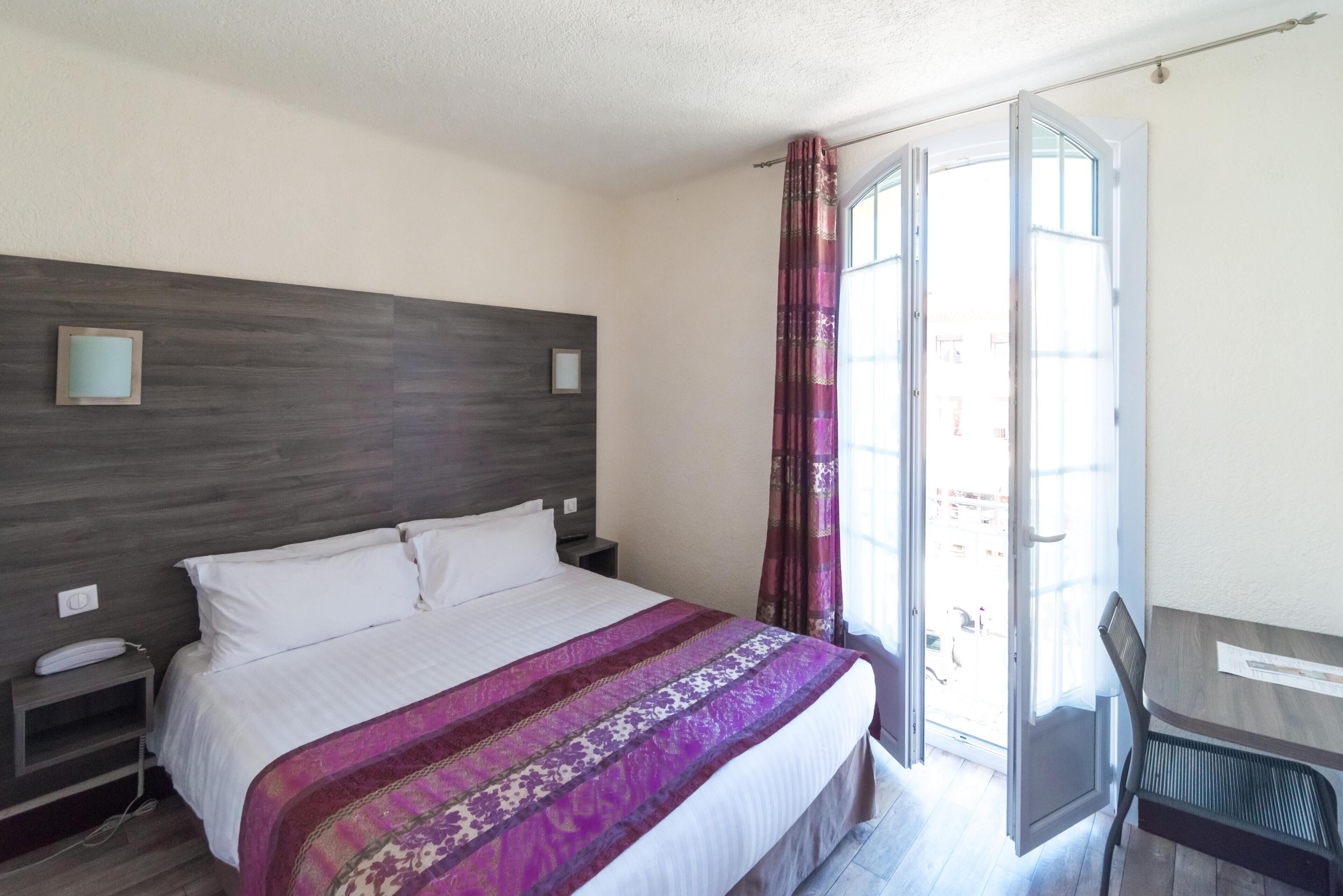 A hotel room with a bed, a nightstand, a desk, and a chair.