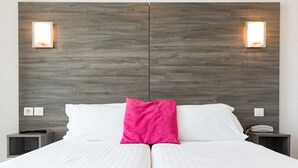 A double bed with white linens and a bright pink pillow, flanked by two nightstands with a phone and a lamp on each. - Le 21 Hotel (Saint-Raphael)