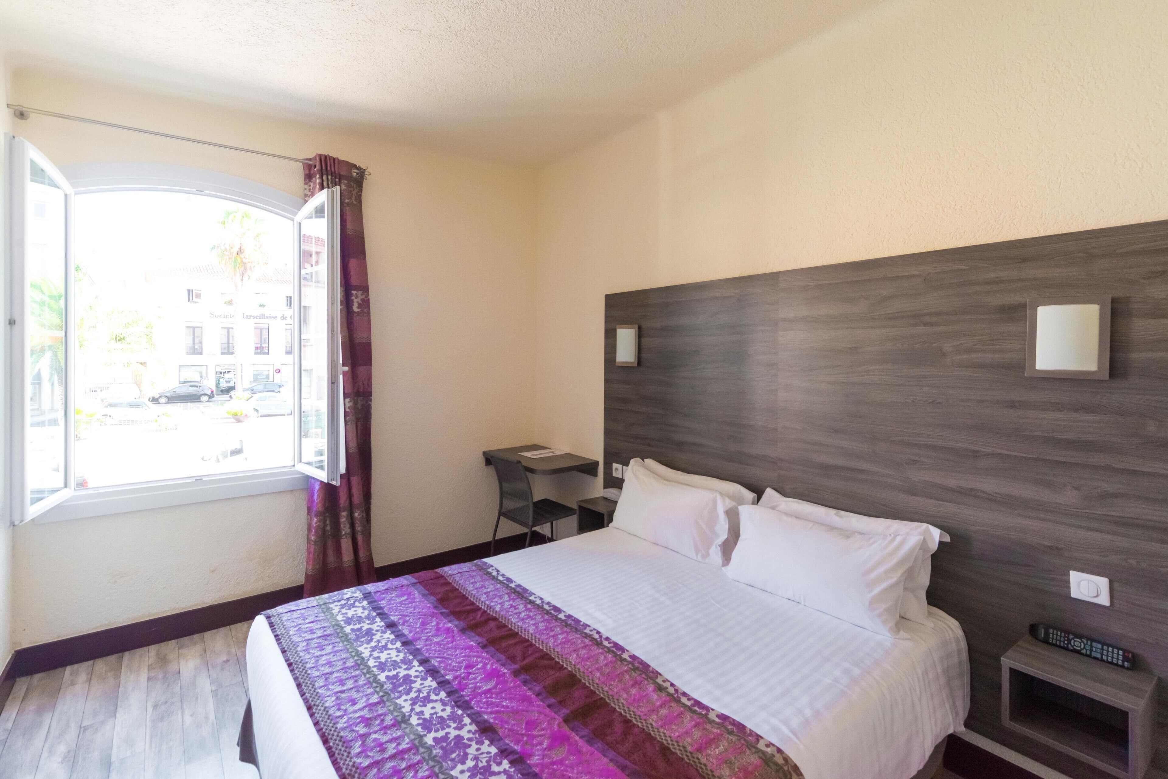 Habitación de hotel con cama, escritorio, silla, ventana con cortinas y vista a la calle.