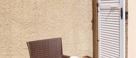 Un área de comedor al aire libre con mobiliario de mimbre, una mesa servida con platos, tazas y una cesta de comida.