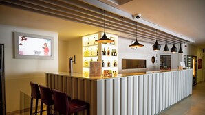 Zona de bar con mostrador, taburetes, iluminación colgante y una pantalla de televisión.